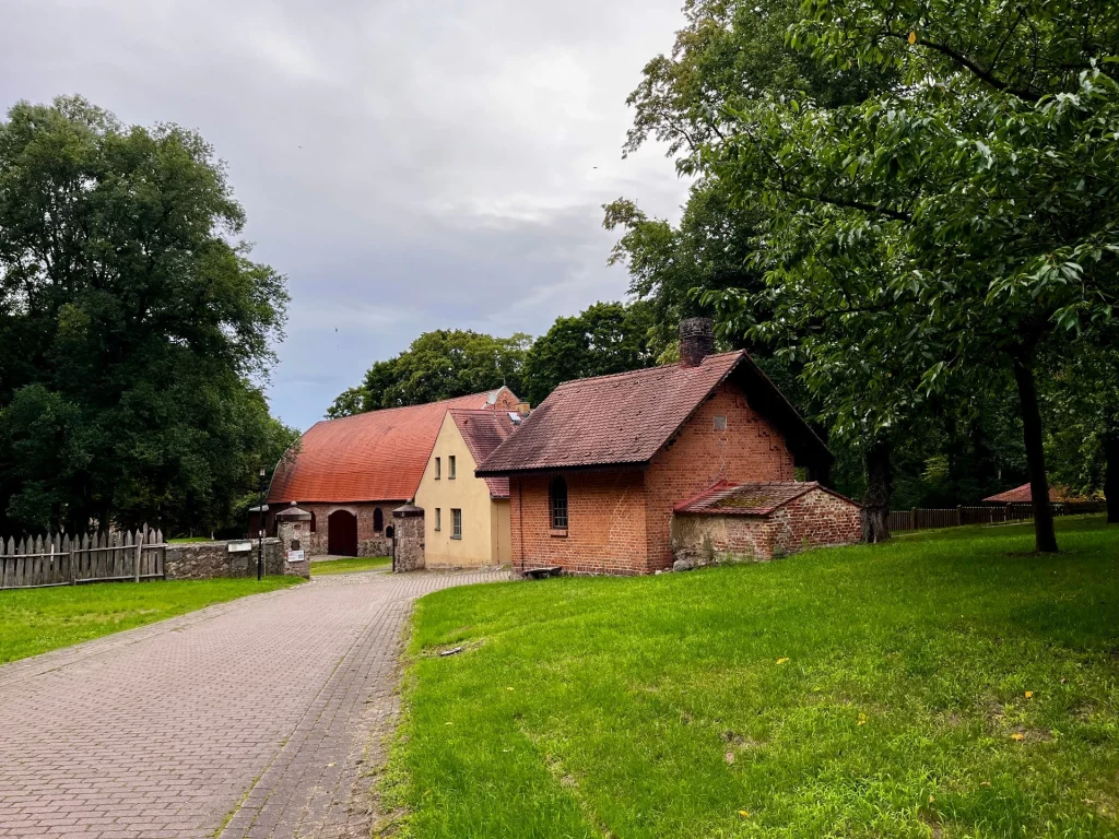 Ein gepflasterter Weg führt auf ein idyllisches Ensemble aus Backsteingebäuden und einer großen Scheune auf dem Burggelände zu.