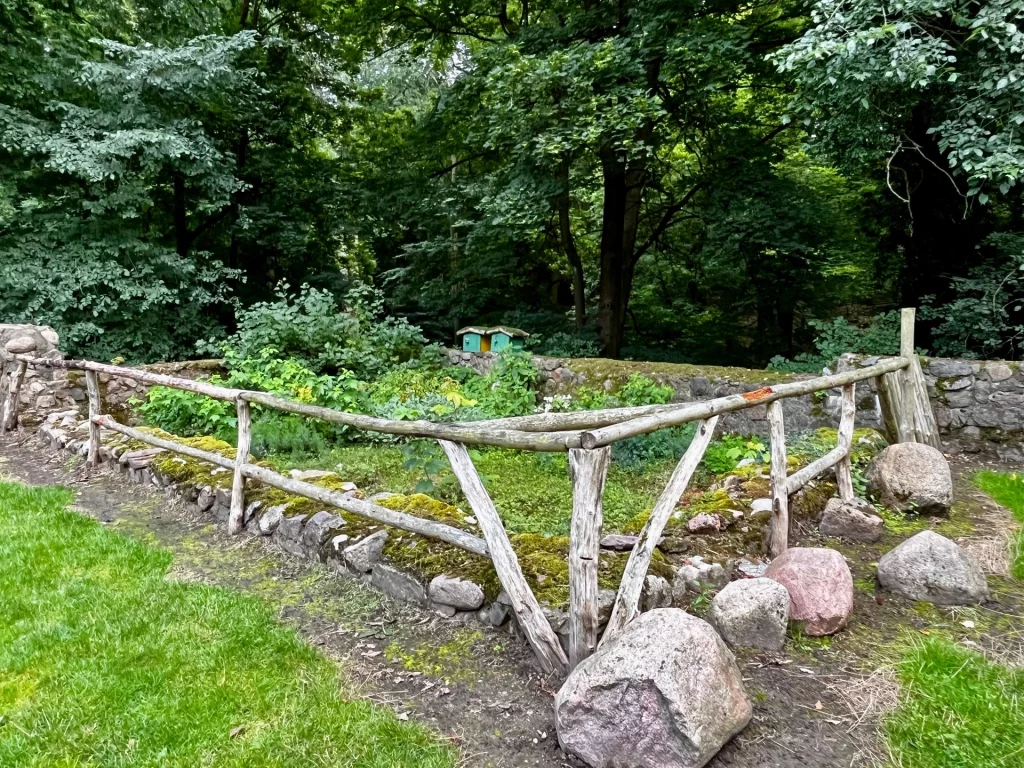 Ein mit einem rustikalen Holzzaun eingefasster Kräutergarten vor einer alten Feldsteinmauer im Waldgebiet der Burg.