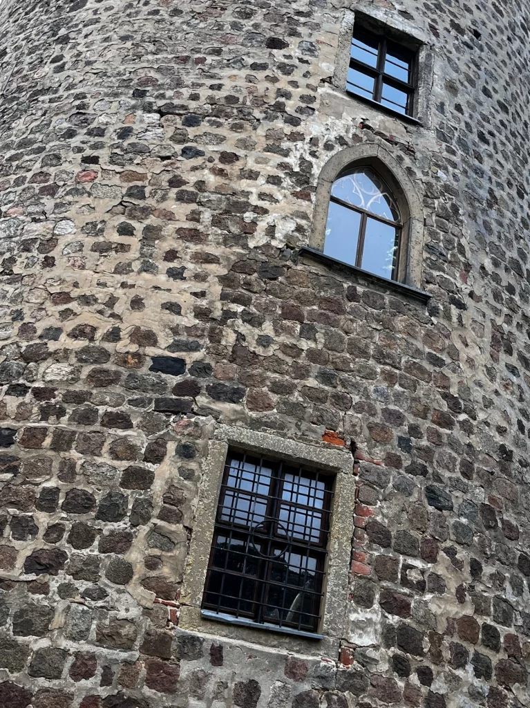 Detailaufnahme der rauen Natursteinwand eines Burgturms mit drei übereinander liegenden Fenstern, darunter ein elegantes spitzbogiges Fenster.