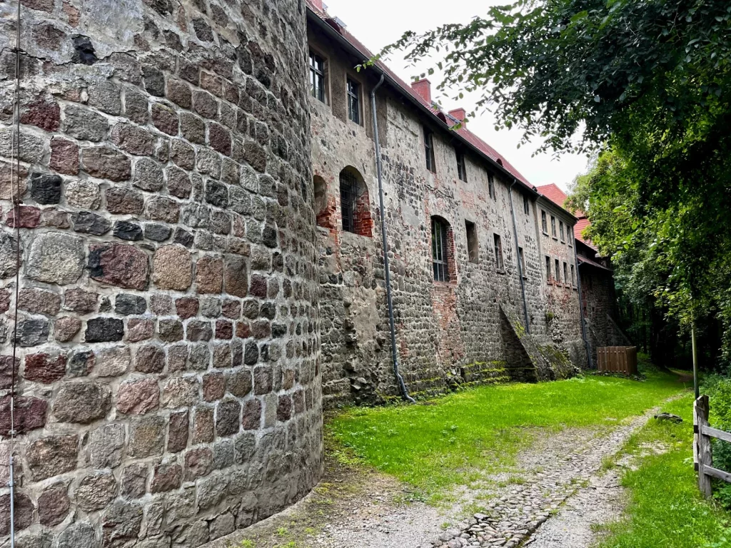 Blick entlang der historischen Außenmauer der Burg Rabenstein mit verschiedenen Fensteröffnungen und einem gepflasterten Wanderweg im Vordergrund.