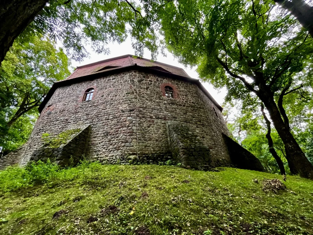 Froschperspektive auf ein achteckiges, steinernes Turmgebäude der Burg Rabenstein, das von dichten, grünen Baumkronen eingerahmt wird.