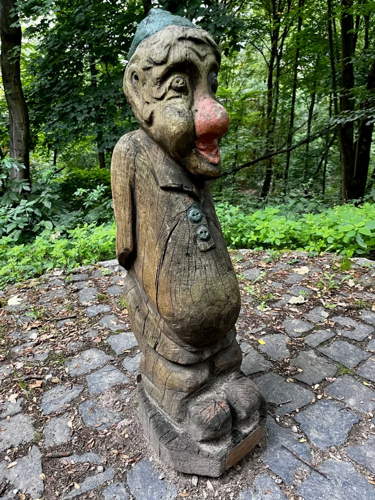 Eine amüsante, aus Holz geschnitzte Kobold-Figur mit roter Nase und blauer Mütze am Wegesrand der Burg Rabenstein.
