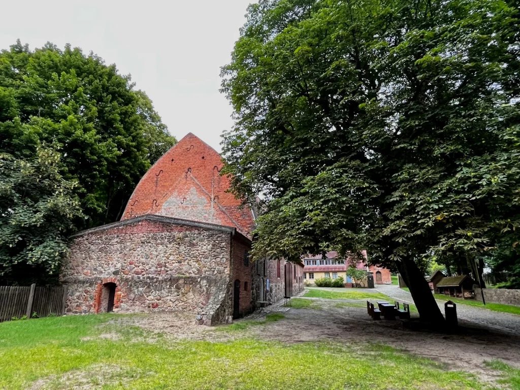 Historisches Wirtschaftsgebäude aus Backstein und Feldstein auf dem Burggelände unter einem großen, ausladenden Laubbaum.