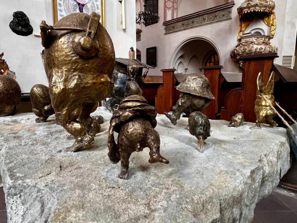 Installation aus mehreren kleinen Bronzefiguren auf einem großen Steinblock, dargestellt als märchenhafte, zwergenartige Gestalten in Bewegung.