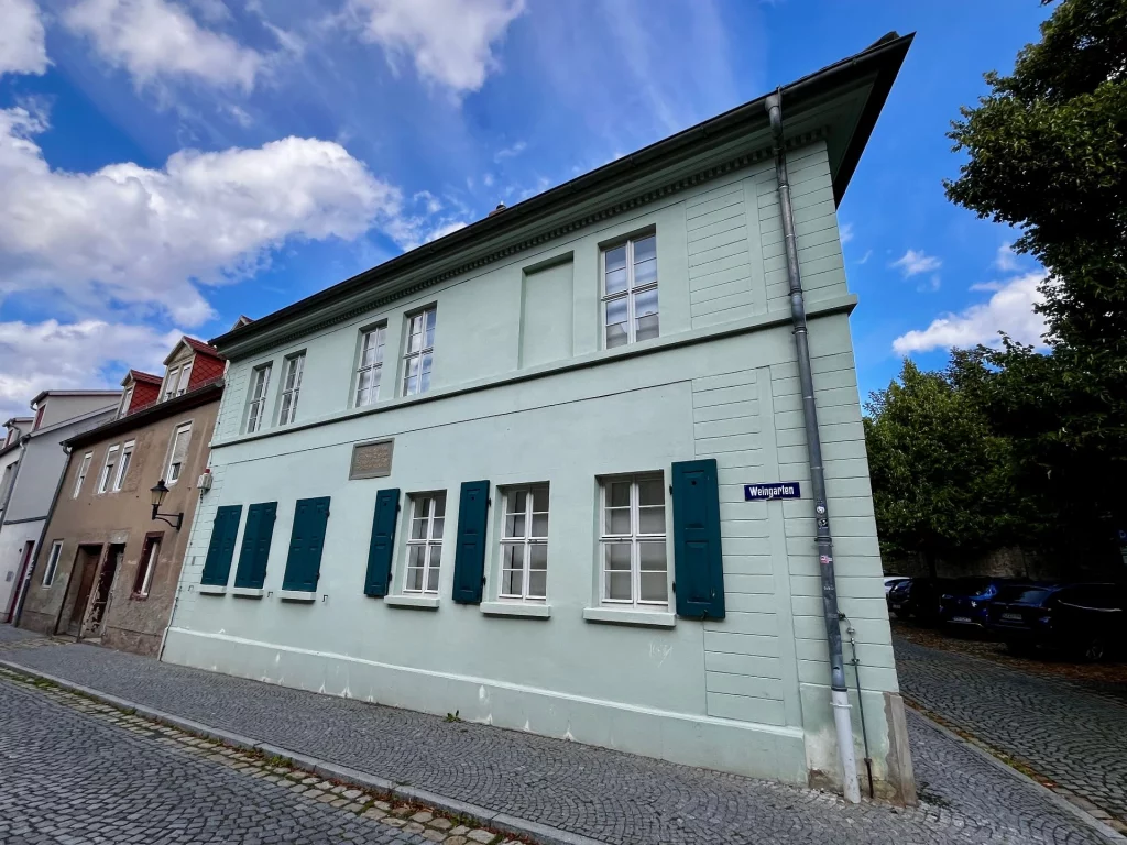 Ein hellgrünes, klassizistisches Eckhaus mit dunkelgrünen Fensterläden in der Straße „Weingarten“. Eine kleine Gedenktafel an der Fassade weist es als ehemaligen Wohnort von Friedrich Nietzsche aus.