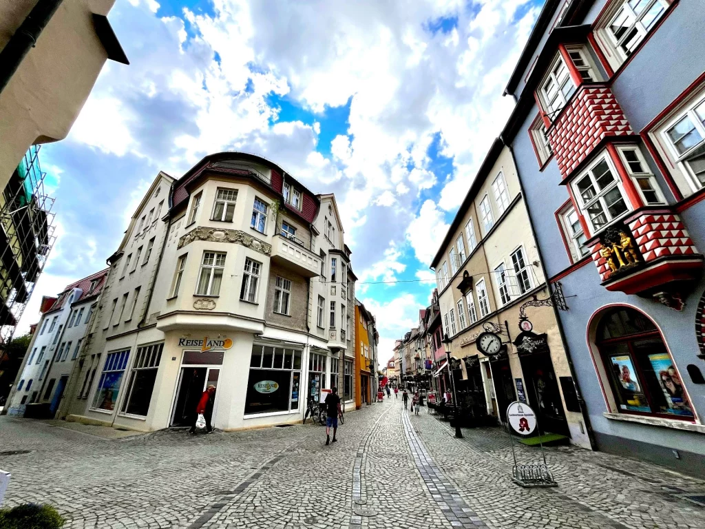 Blick in eine Altstadtstraße mit Kopfsteinpflaster, historischen Häusern, Geschäften und dramatischem Wolkenhimmel.