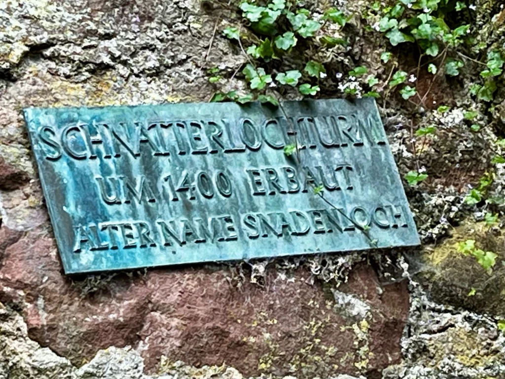 Eine grünlich patinierte Metalltafel an einer Steinwand mit der Inschrift: „Schnatterlochturm um 1400 erbaut. Alter Name Snadenloch.“