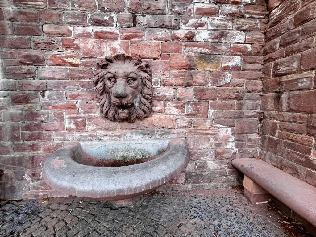 Historischer Brunnen mit Löwenkopf aus Sandstein vor Backsteinwand. 