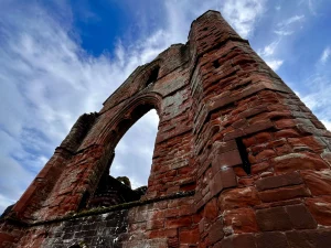 Historisches Mauerwerk der Sweetheart Abbey bei Dumfries: Nahaufnahme der Turmruine aus rotem Sandstein mit Details der mittelalterlichen Architektur.