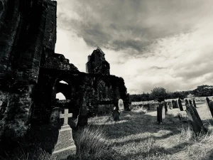in helles, kleines Steinkreuz im Vordergrund, das einen starken Kontrast zu den tiefschwarzen Schatten der zerfallenen Abbey-Mauern im Hintergrund bildet.