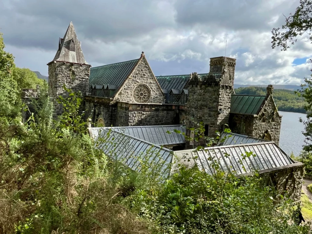 Erhöhte Ansicht der Steinkirche mit ihren markanten grünen Metalldächern, eingebettet in Bäume direkt am Ufer eines Sees.
