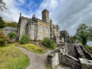 Eine weitwinklige Außenansicht der St Conan’s Kirk, einer eklektischen Steinkirche mit verschiedenen Türmen und Anbauten auf einem Hügel unter bewölktem Himmel.
