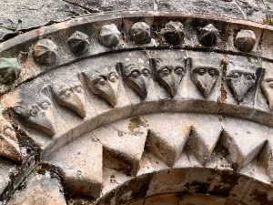 Nahaufnahme eines steinernen Bogens über einer Tür, verziert mit einer Reihe von geschnitzten, vogelähnlichen Gesichtern.