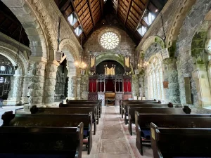 Der Innenraum der Kirche mit hölzernen Kirchenbänken, massiven Steinbögen und einer hohen Holzdecke. Im Hintergrund ist eine Orgel und ein rundes Rosettenfenster zu sehen.