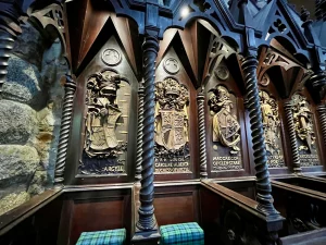 Detailaufnahme von dunklen Holzschnitzereien an der Wand, die heraldische Wappen und Namen schottischer Adliger zeigen.