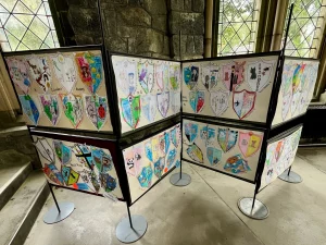 Mehrere Klapptafeln in der Kirche, an denen bunte, von Kindern gemalte Papierwappen befestigt sind.