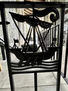 Eine Nahaufnahme eines schwarzen Eisen-Gitters, das ein stilisiertes Ruderschiff auf Wellen darstellt.