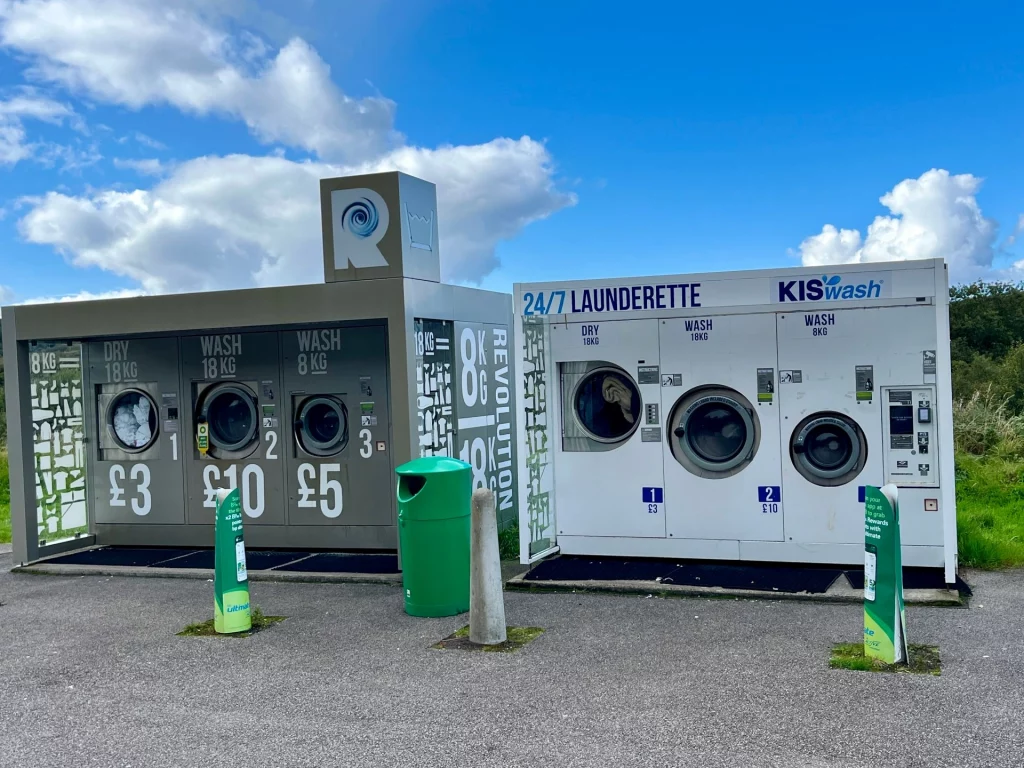 Ein Außenbereich mit modernen, blauen Waschmaschinen und Trocknern zur Selbstbedienung.