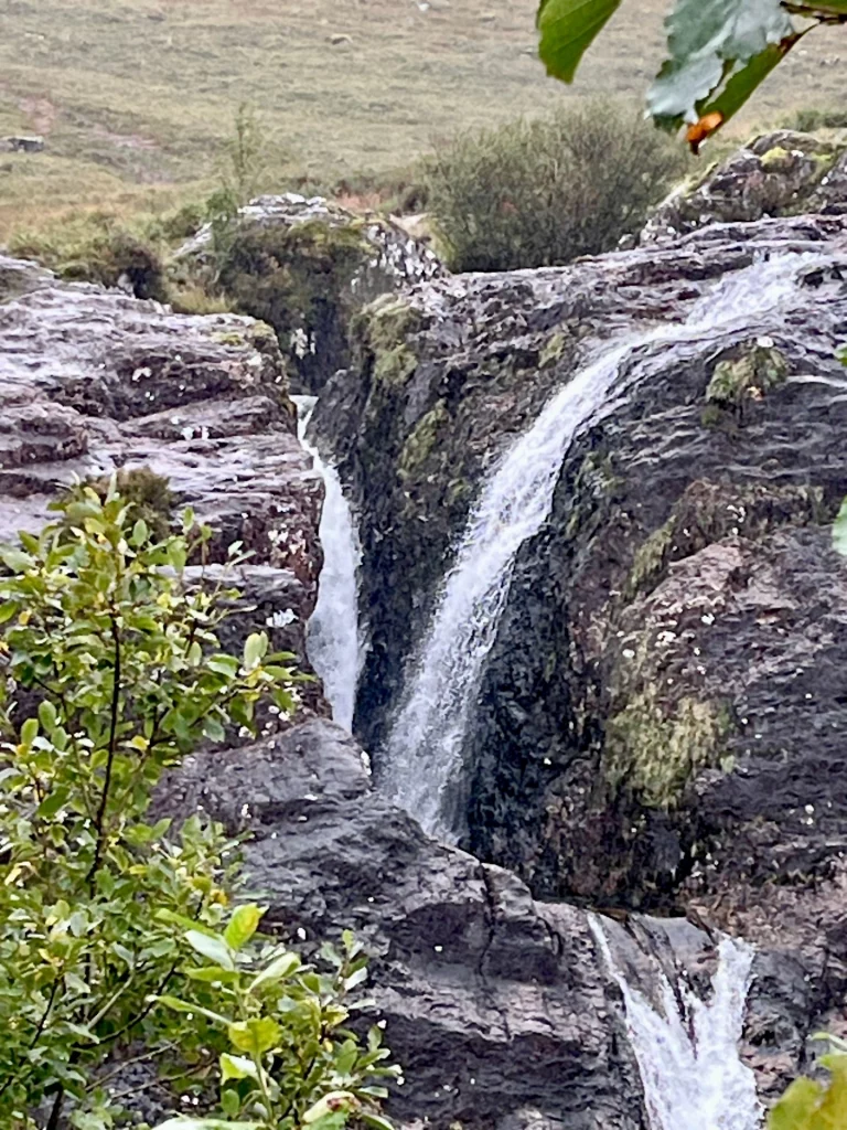 Ein kleiner Wasserfall, der über dunkle, nasse Felsen in eine Schlucht in Glencoe stürzt.