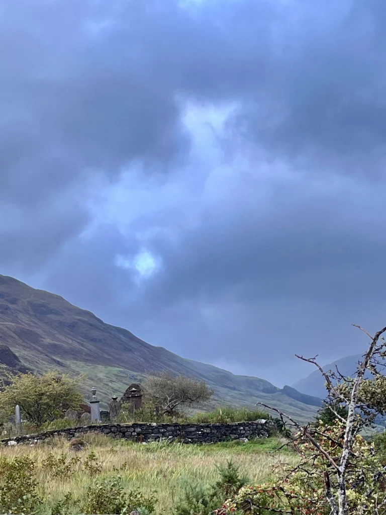 Eine weitläufige Ansicht derselben Ruine, die die dramatische Wolkenstimmung betont. Das dunkle Blau der Wolken bricht über dem Tal auf, während die hügelige Landschaft im Hintergrund in sanftem Licht liegt.