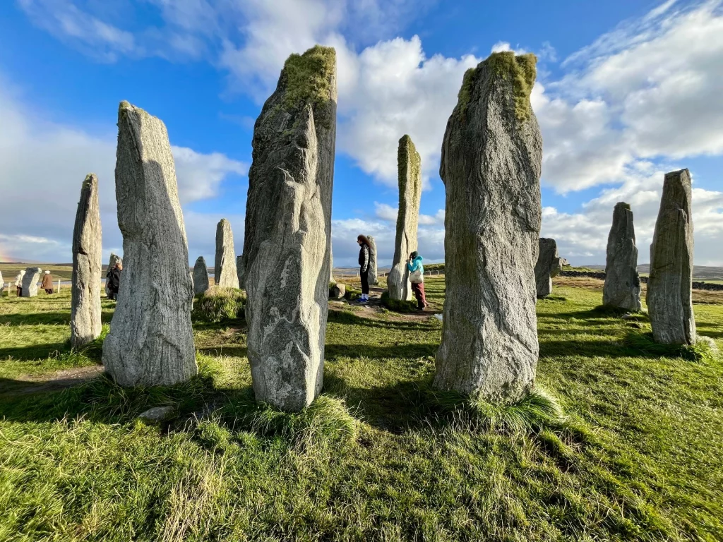 Nahaufnahme mehrerer massiver, moosbewachsener Steine des Callanish-Kreises, zwischen denen Besucher die Dimensionen der Anlage erkunden.
