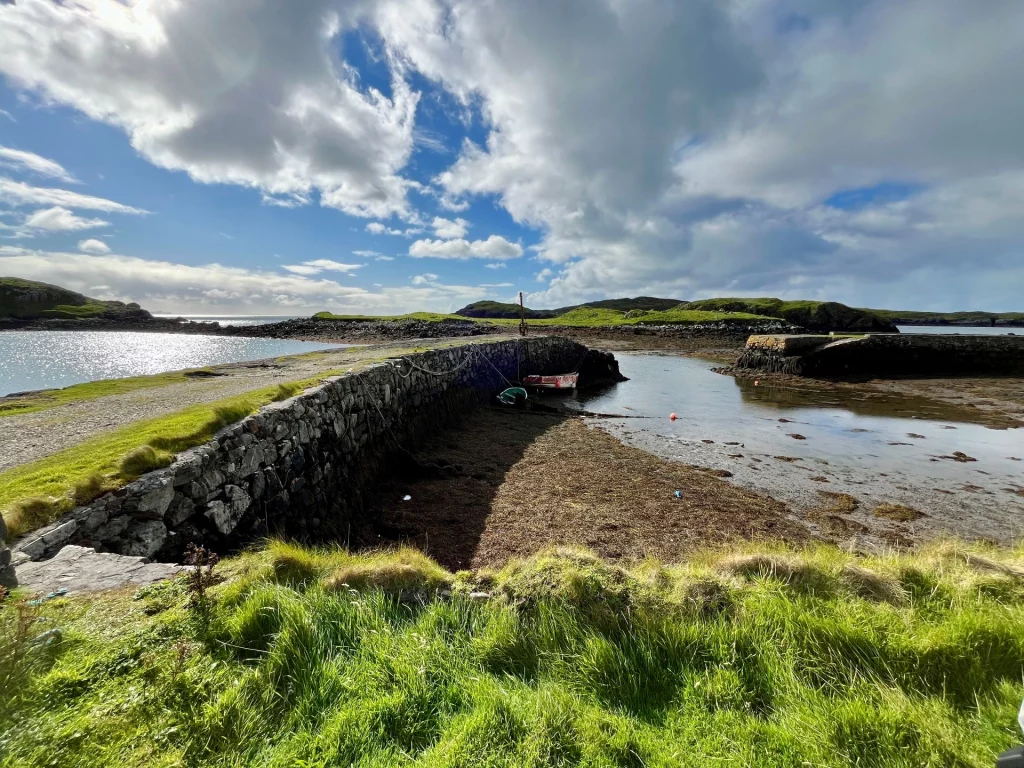 Eine rustikale Steinmauer säumt einen Küstenweg an einer flachen Bucht bei Ebbe unter dramatischem Wolkenhimmel.