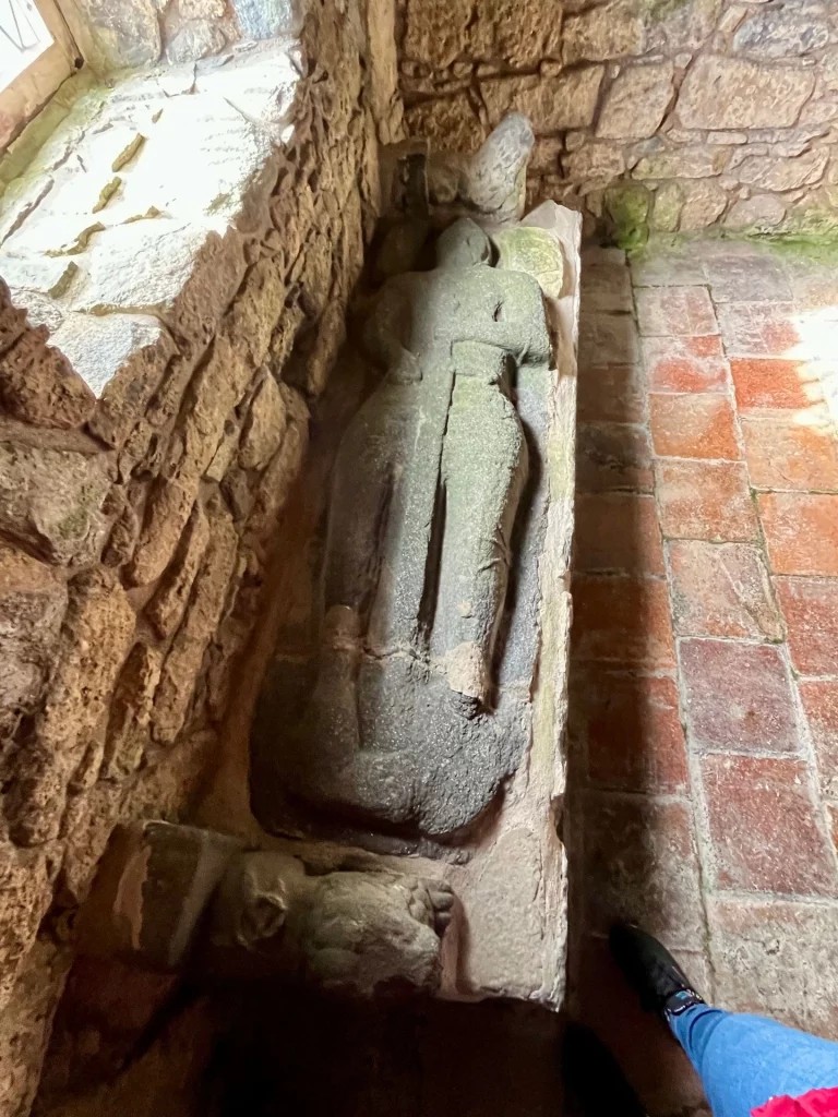 Nahaufnahme eines mittelalterlichen Steinsarkophags mit der verwitterten Skulptur eines liegenden Ritters (Effigie) in voller Rüstung.