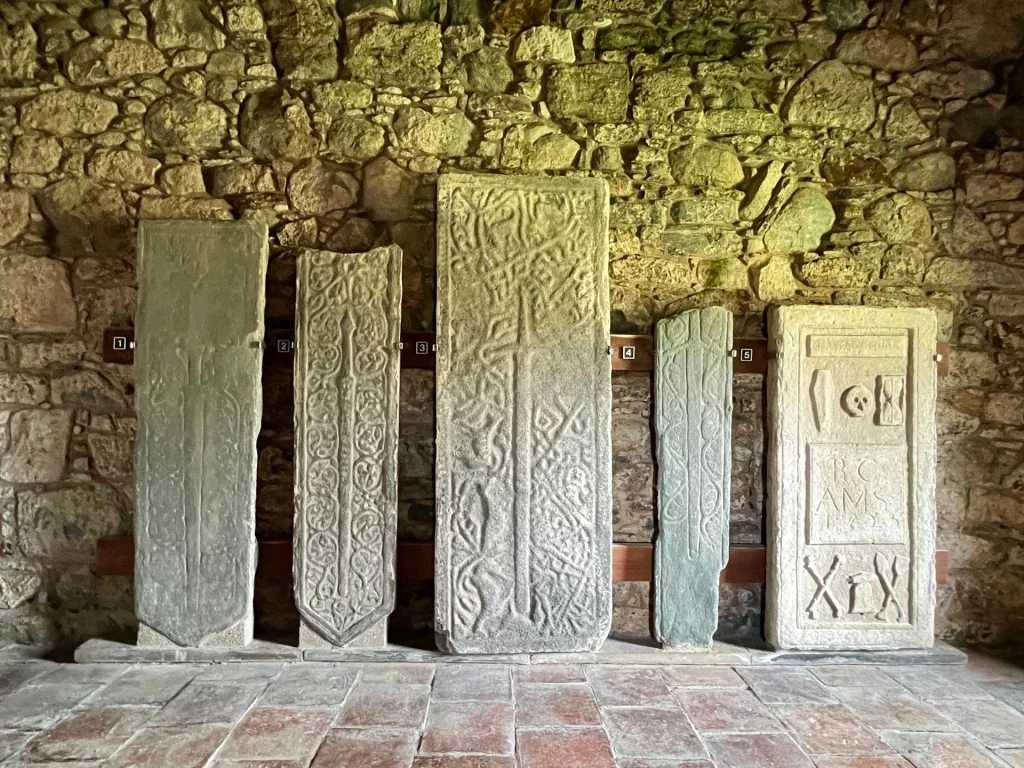 Fünf hochkant aufgestellte, mittelalterliche Grabplatten aus Stein vor einer Mauer in der St. Clement’s Church, verziert mit Reliefs von Schwertern und keltischen Ornamenten.