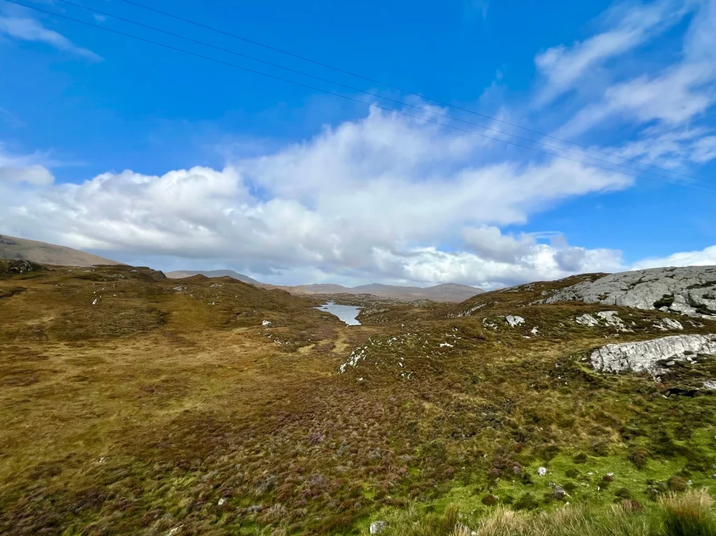 Eine weite, unberührte Moorlandschaft in herbstlichen Braun- und Grüntönen, die sich zwischen sanften Hügeln und kleinen Wasserstellen erstreckt.
