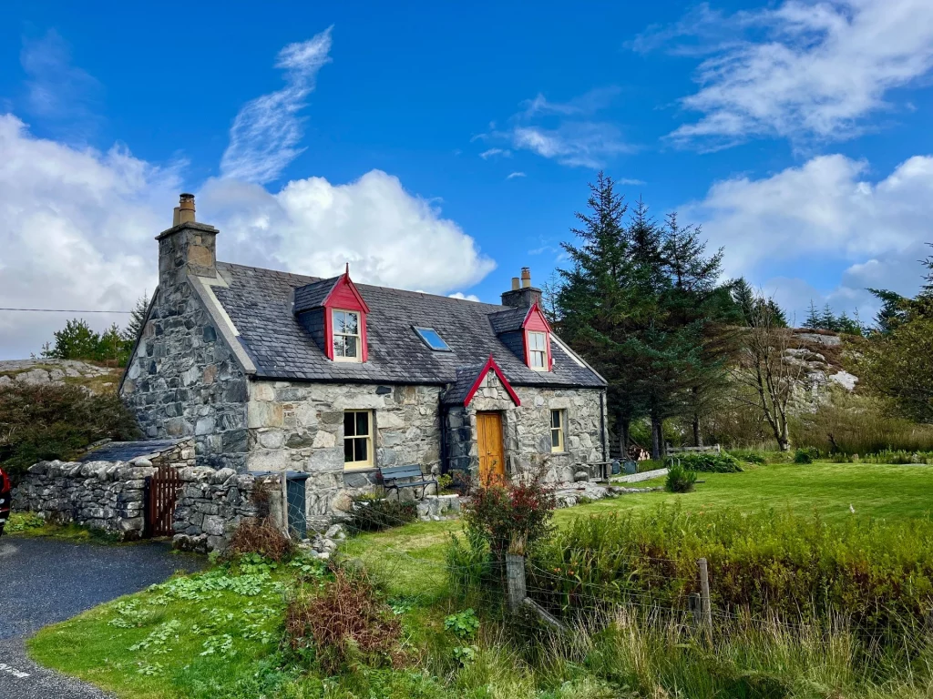 Ein traditionelles schottisches Steinhaus mit markanten roten Dachgauben und einem gepflegten Garten. Das Cottage fügt sich harmonisch in die umliegende Hügellandschaft ein.