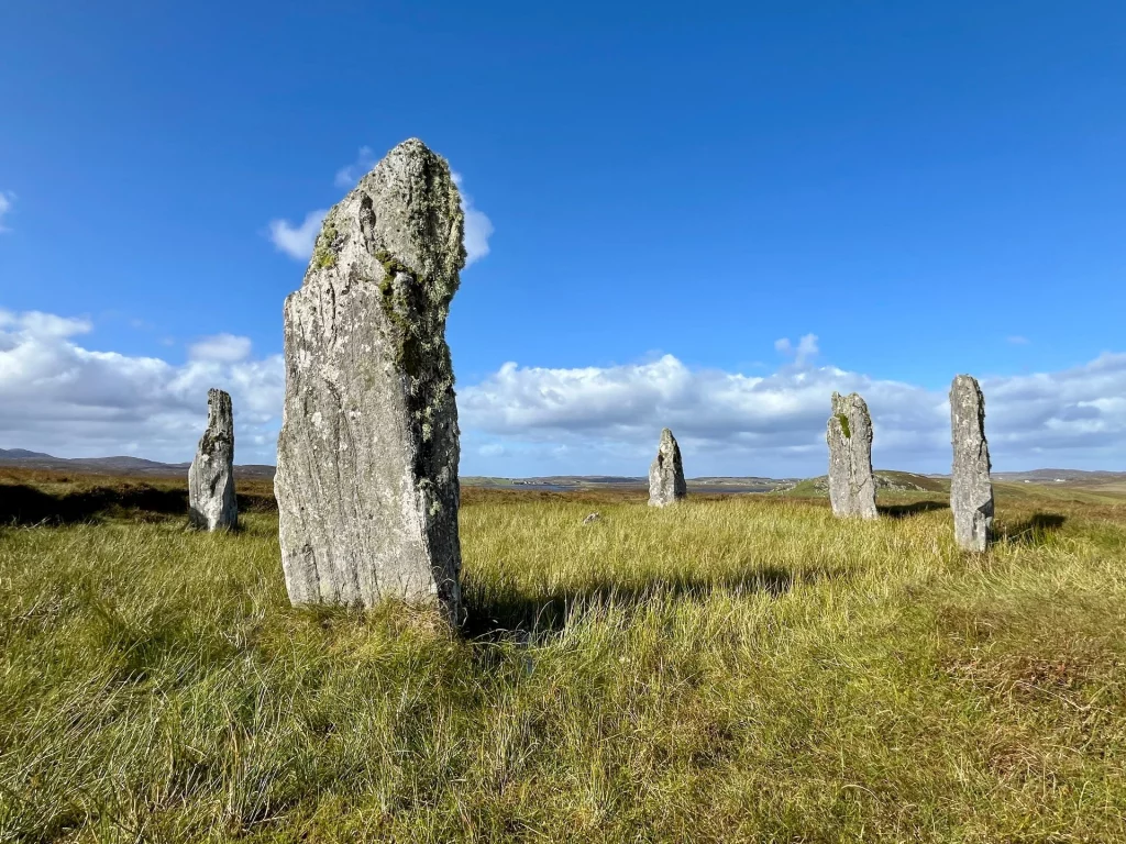 Callanish VII Steinkreis Cnoc Fhillibhir Bheag Hebriden: Nahaufnahme eines großen, aufrecht stehenden Steins eines Steinkreises vor einem strahlend blauen Himmel mit vereinzelten Wolken.