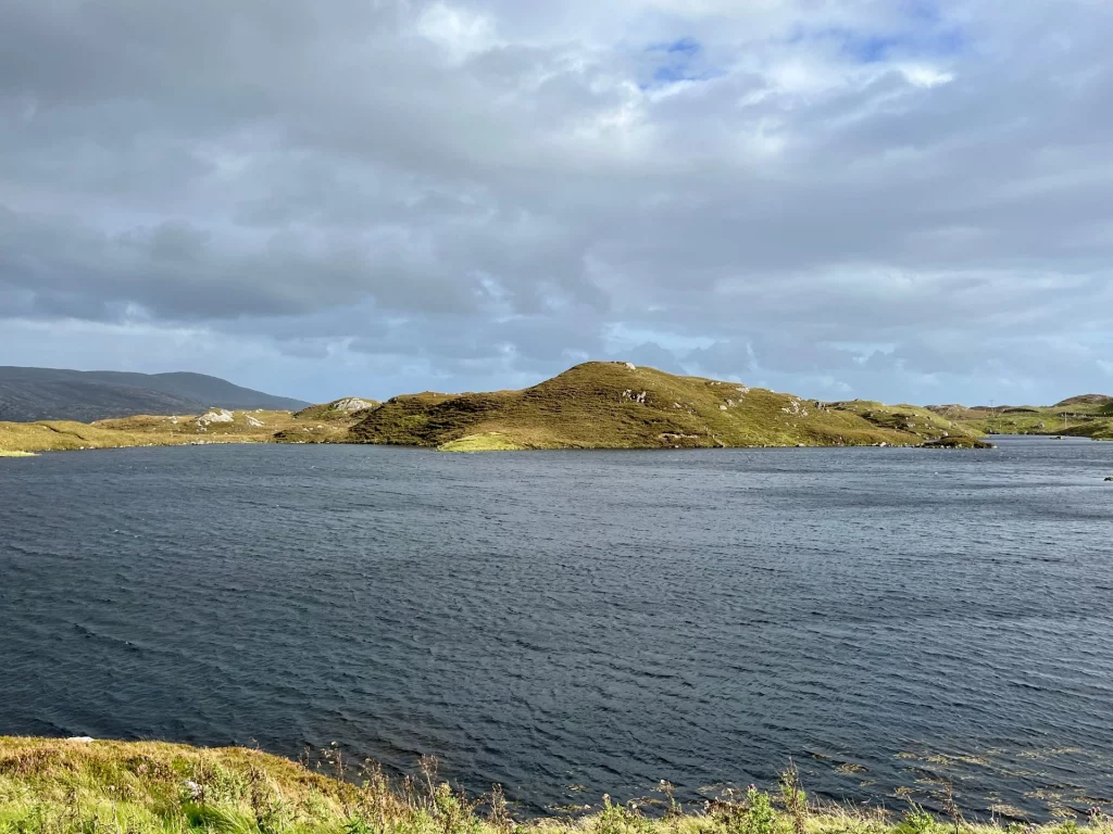 Ein dunkler Süßwassersee (Loch) in der kargen, hügeligen Moorlandschaft der Isle of Harris unter dramatischem Wolkenhimmel.
