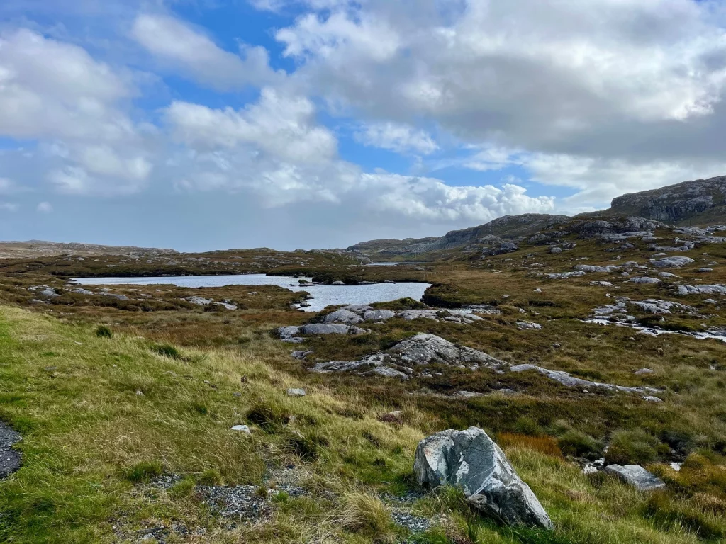Weite, felsige Hebriden-Landschaft mit kleinen Wasserstellen und grünen Moosflächen während einer Wanderung auf Harris.
