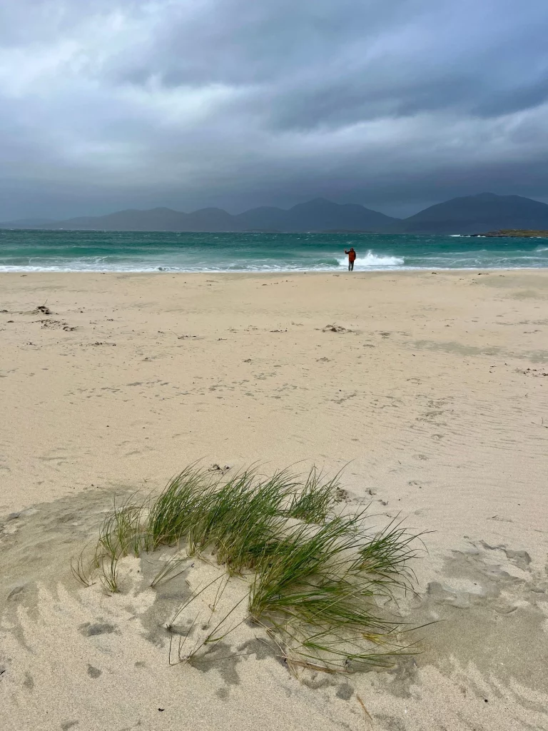 Weiter, heller Sandstrand unter einem bewölkten, dramatischen Himmel mit Dünenhafer im Vordergrund.