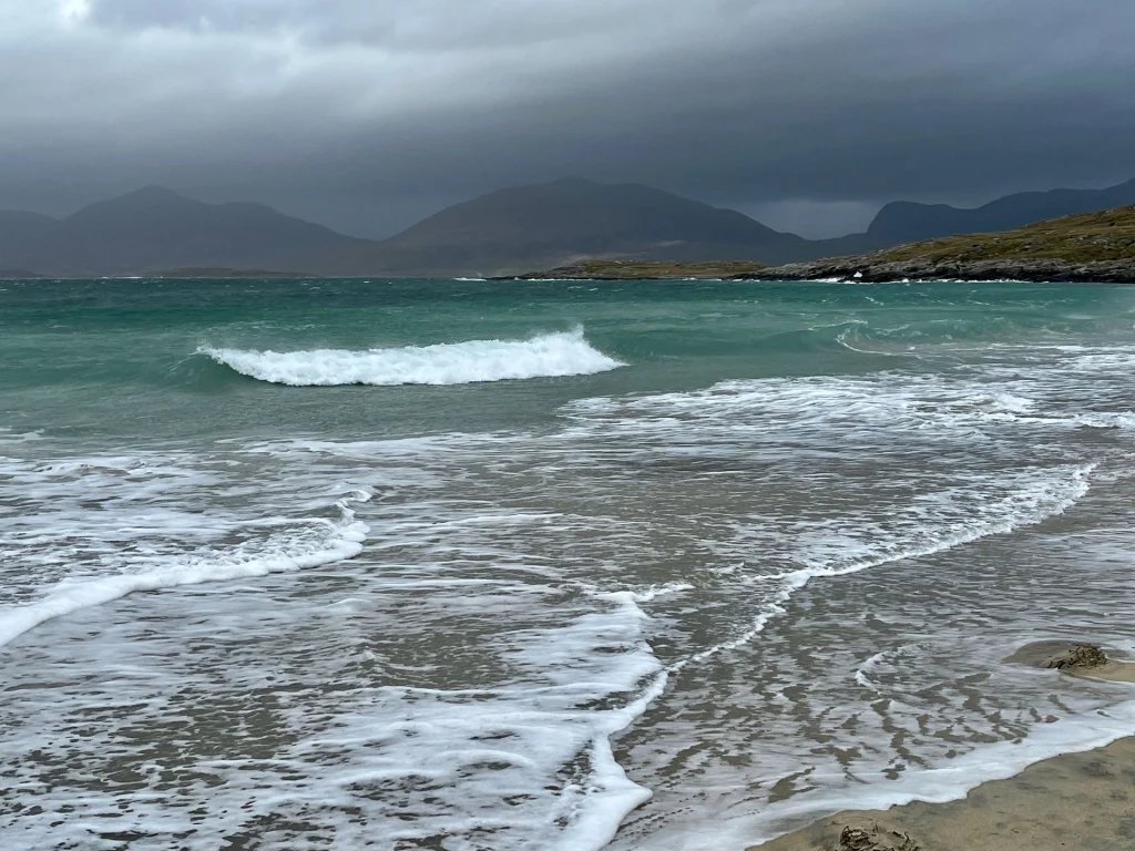 Nahaufnahme von weißen Schaumkronen der Meeresbrandung an einer felsigen Küste unter grauem Himmel.