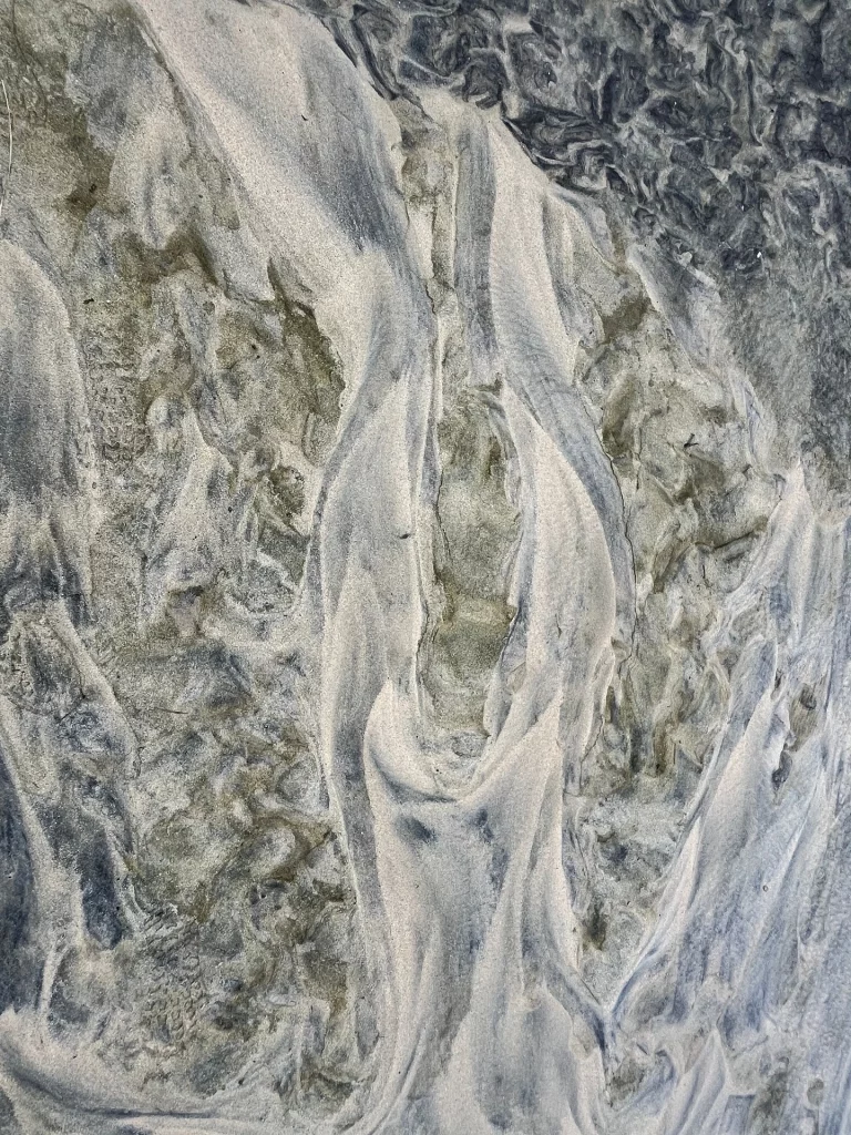 Nahaufnahme von feinen Fließspuren und dunklen Sedimenten im hellen Sand am Ufer von Luskentyre, Schottland.