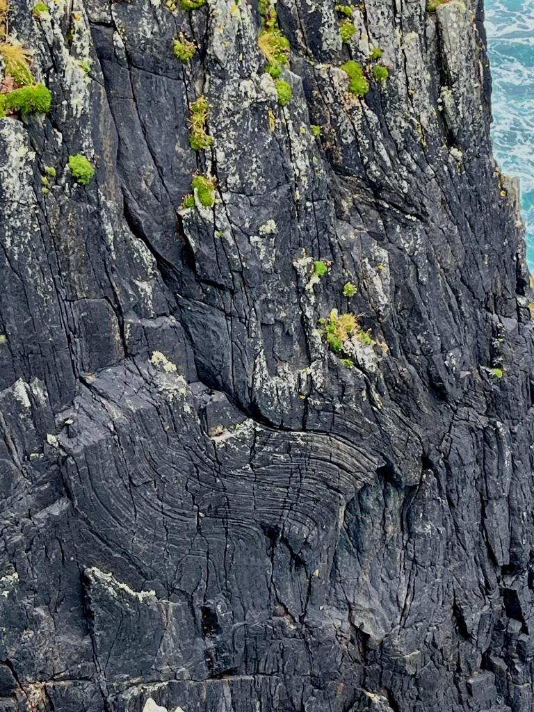 Detailaufnahme einer dunklen, vertikal zerklüfteten Felswand, die die Jahrmillionen alte, geologische Struktur der Hebriden zeigt.