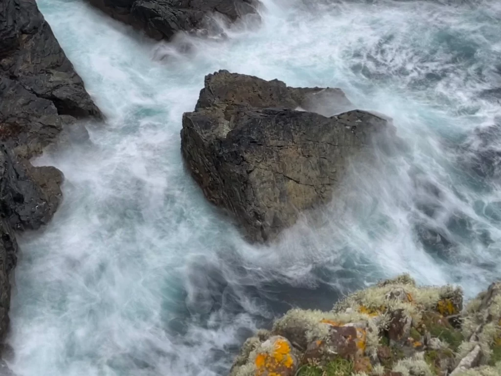 Langzeitbelichtung von Meereswellen, die weiß schäumend um dunkle Felsen im Ozean spülen.
