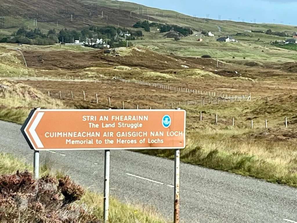 Ein braunes Hinweisschild am Straßenrand mit der Aufschrift „The Land Struggle / Cuimhneachan Nan Gaisgeach“ (Denkmal für die Helden des Landes).