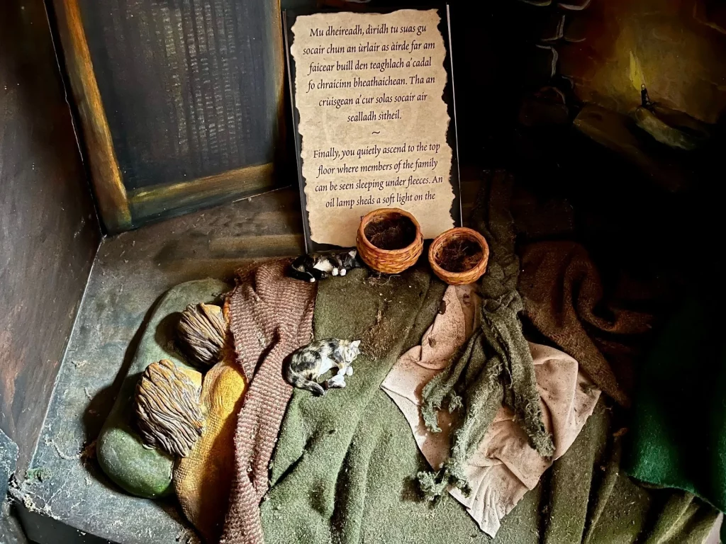 Ein Ausstellungsstück mit einem Text auf pergamentähnlichem Papier, davor platziert sind kleine geflochtene Schalen und Stoffproben auf einem steinigen Untergrund.