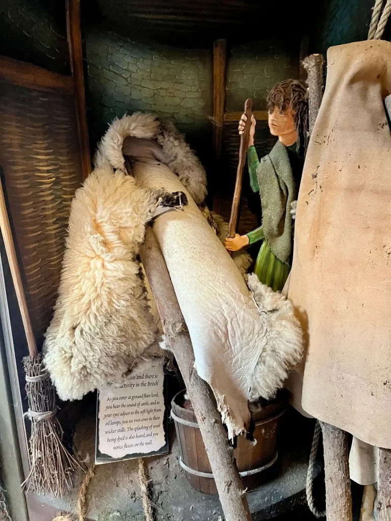 Eine museale Darstellung zeigt rustikale Alltagsgegenstände der Eisenzeit, darunter Tierfelle, Holzstäbe und grobe Textilien.