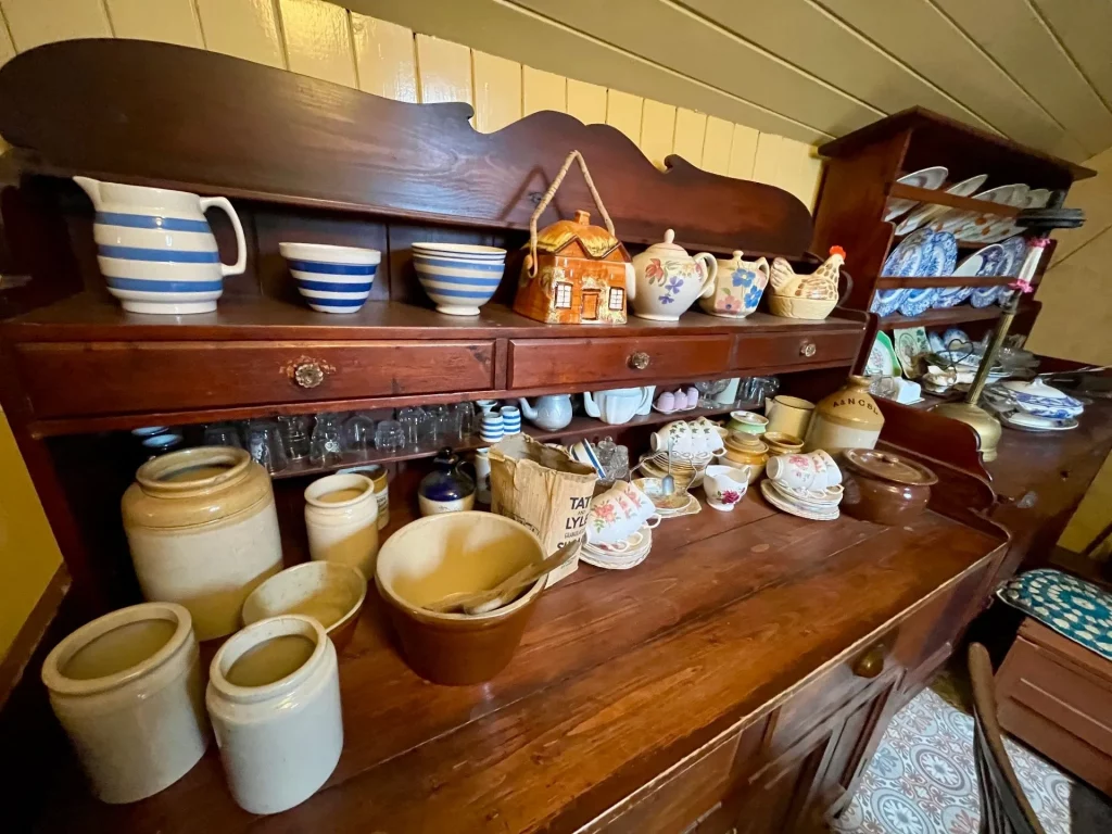 Ein rustikales Küchenbuffet aus dunklem Holz, bestückt mit verschiedenen Keramikschüsseln, Teekannen und Vorratsgefäßen in einem historischen Blackhouse.