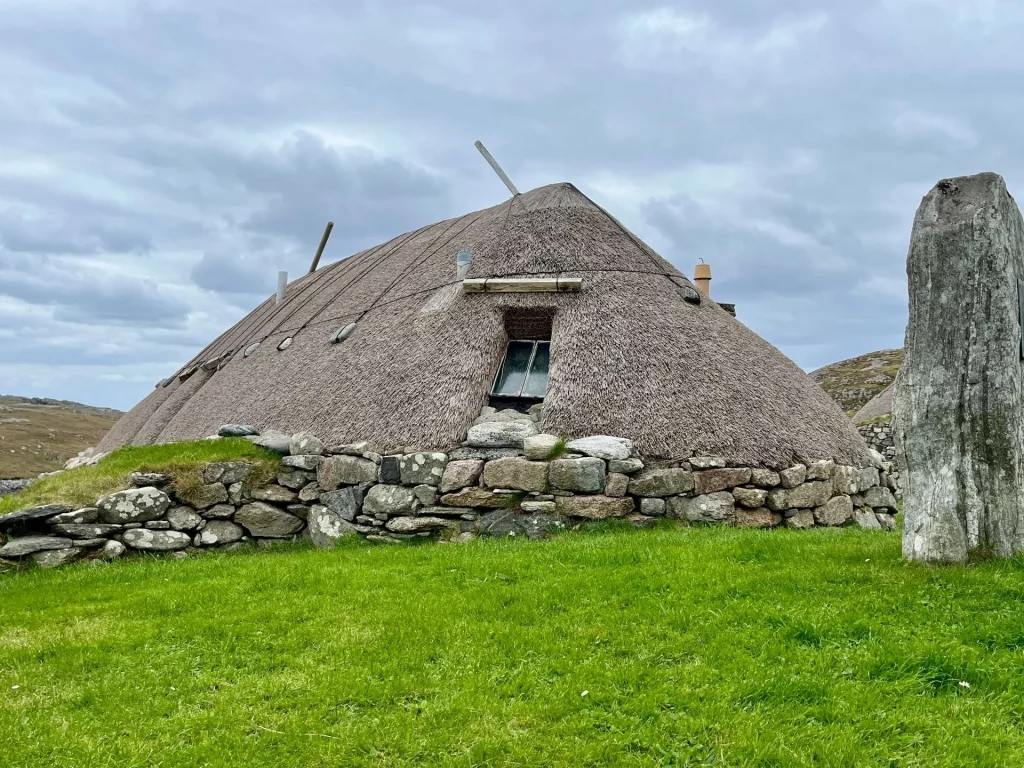 Außenansicht eines historischen Blackhouses in Na Gearrannan mit charakteristischem, abgerundetem Strohdach und dicken Steinmauern unter bewölktem Himmel.