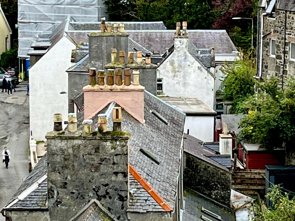 Blick von oben auf die charakteristischen, grauen Schieferdächer und zahlreichen Schornsteine (Chimney Pots) traditioneller Häuser in einer schottischen Ortschaft.