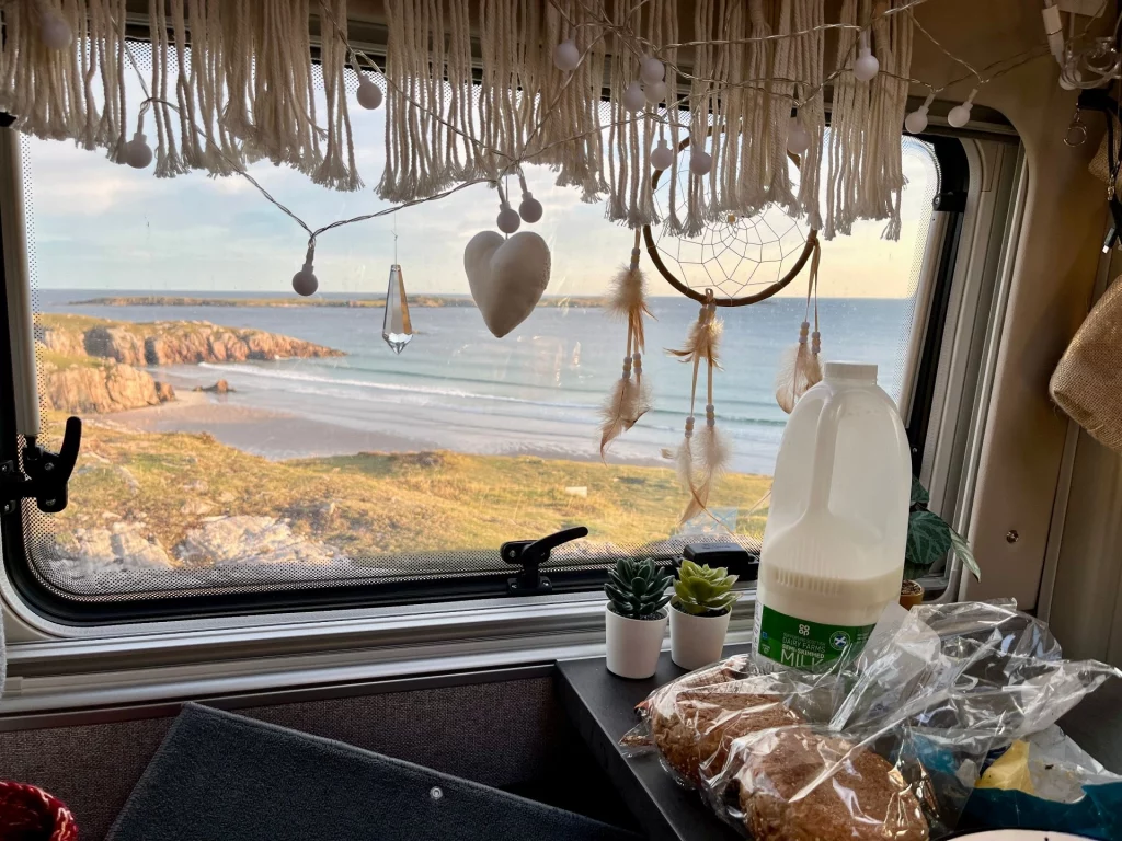 Weite Aussicht von den felsigen Klippen auf den hellen Sandstrand der Sango Bay bei Durness im sanften Morgenlicht, mit Blick auf den ruhigen Nordatlantik und die schottische Küstenlandschaft unter leicht bewölktem Himmel.