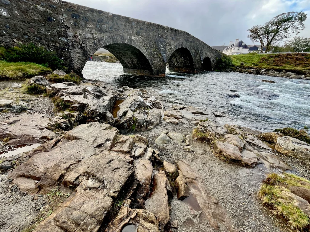 Nahaufnahme des steinernen Bogens der Sligachan Bridge über einem klaren, felsigen Flussbett.