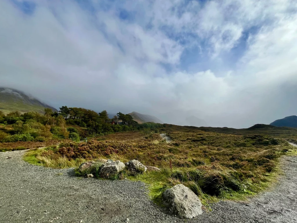 Ein geschwungener Schotterweg führt durch die weite, mit Heidekraut bewachsene Moorlandschaft unter einem wolkenverhangenen Himmel.