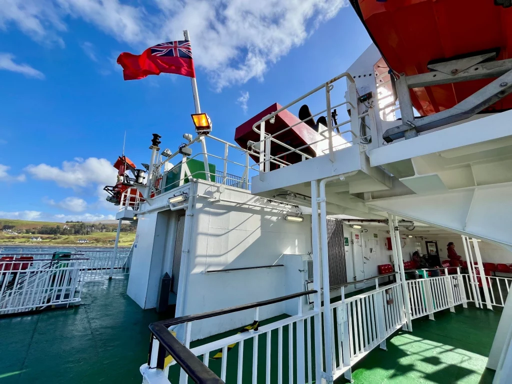 Blick auf das weiße Deck der CalMac-Fähre mit einer wehenden roten Flagge gegen den blauen Himmel.