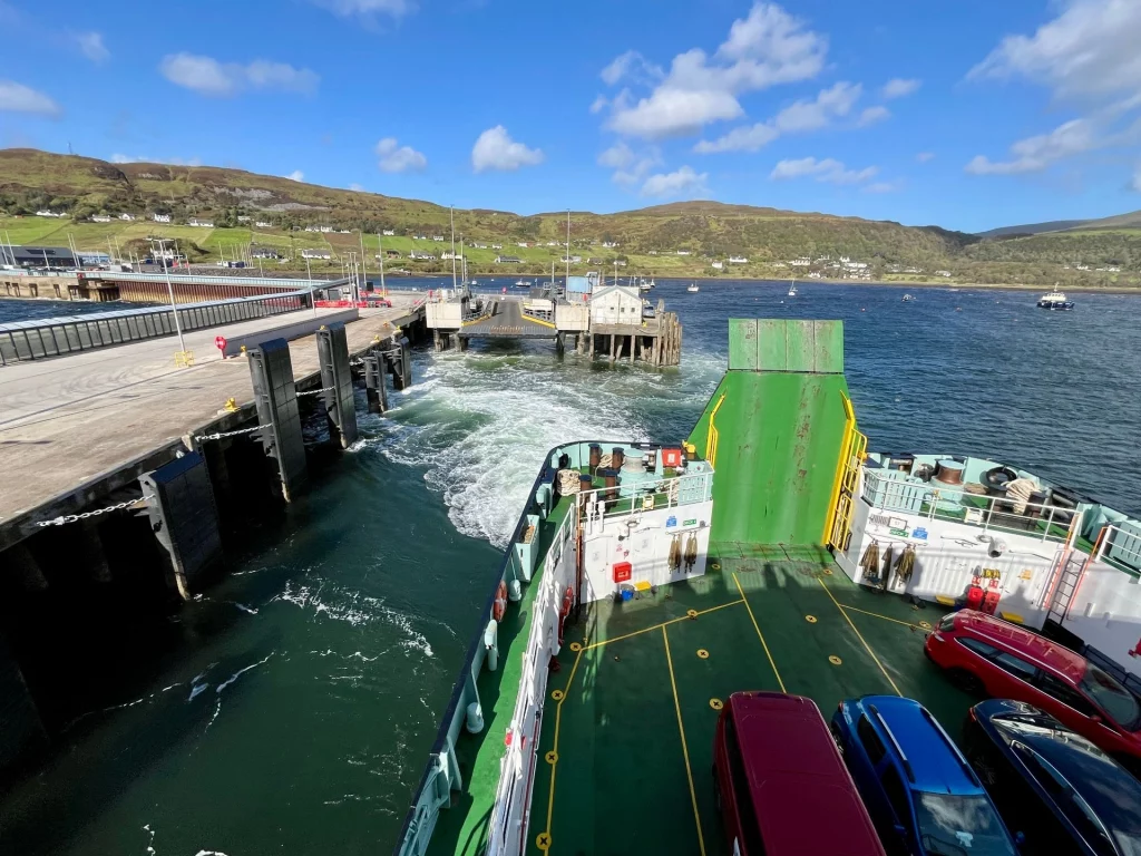 Blick vom Oberdeck der Fähre auf das Parkdeck mit bunten Autos und das aufgewühlte blaue Wasser bei der Ausfahrt aus dem Hafen von Uig.