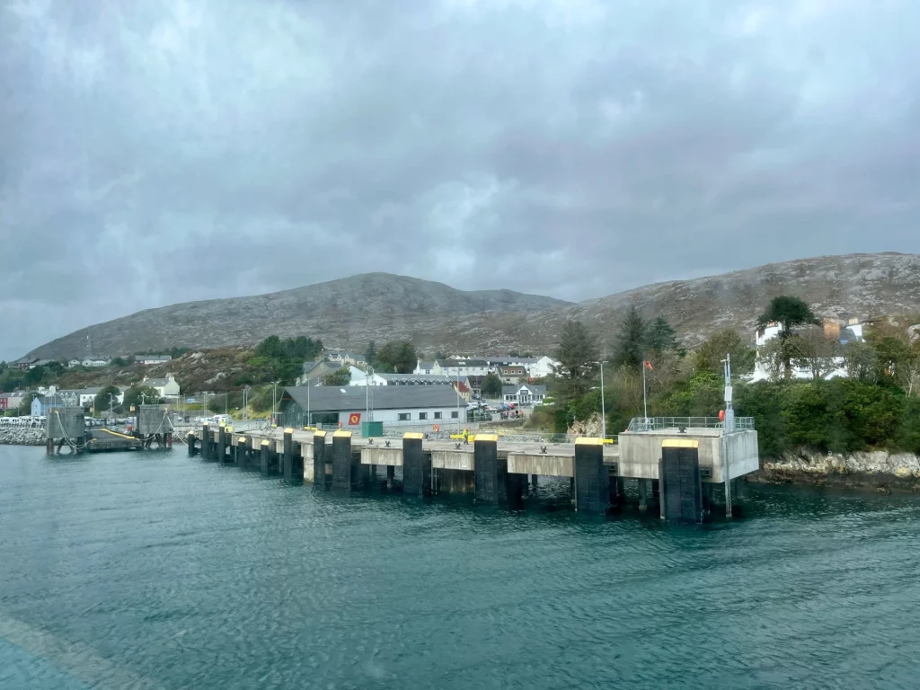 Blick von der Fähre auf die massiven, schwarzen Dalben der Hafenanlage vor einer hügeligen, schottischen Küstenlandschaft unter bewölktem Himmel.